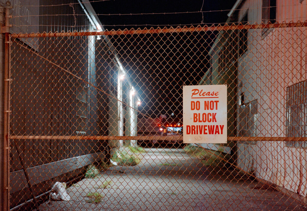 "Please do not block driveway" sign on a gate closing an alley at night.