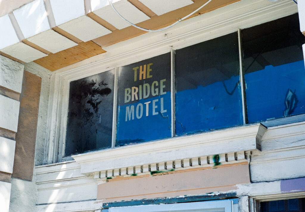 A sign reading "The Bridge Motel" on a beaten down motel front. 